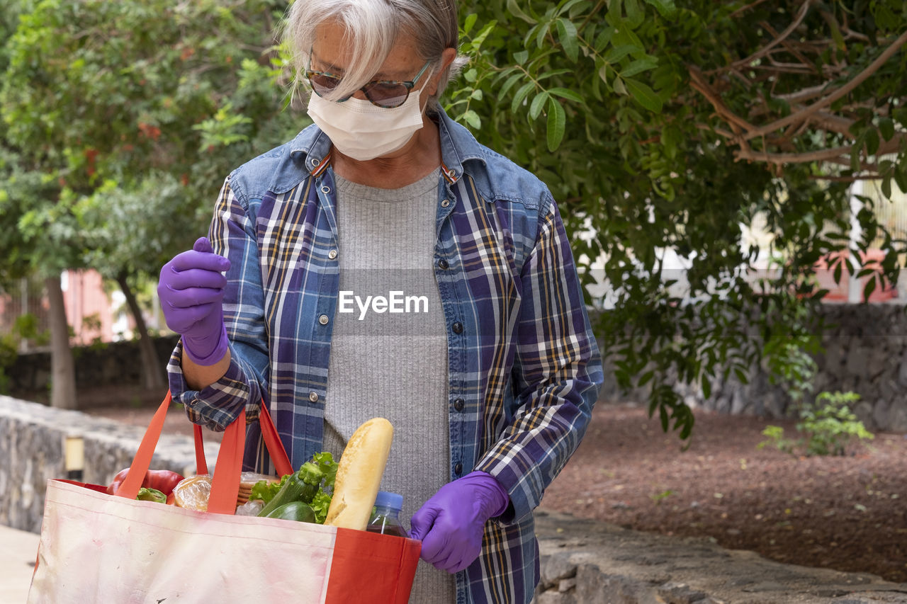 Senior woman holding groceries bag standing by plants