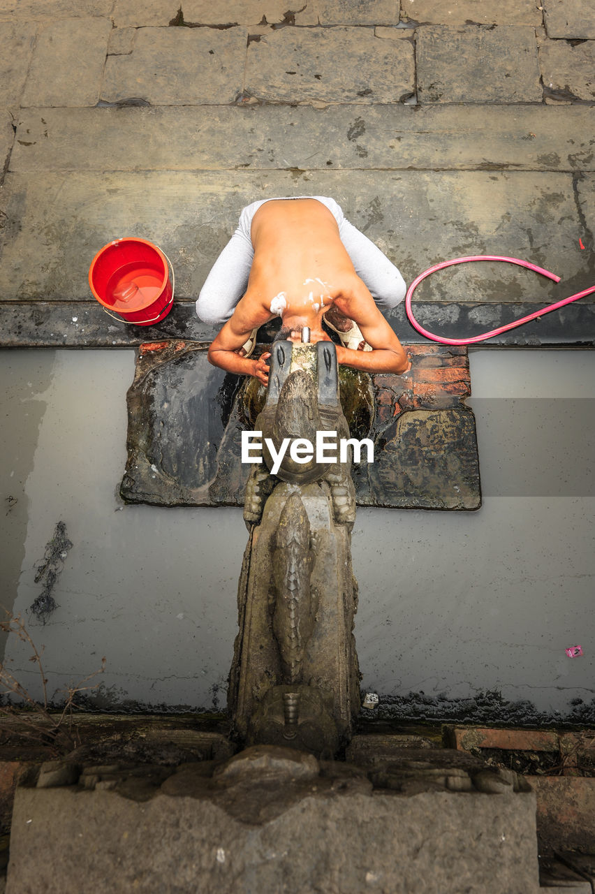 High angle view of man bathing from water fountain at temple