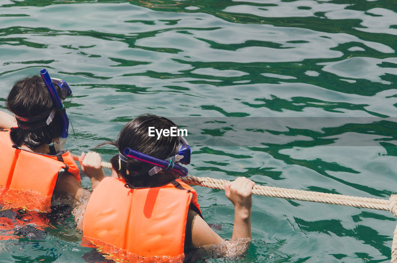 Rear view of people holding rope while snorkeling in sea