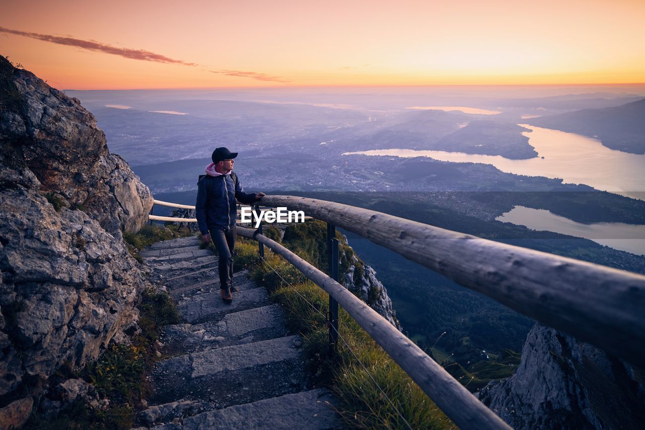 Man looking away while standing on steps against sky during sunset