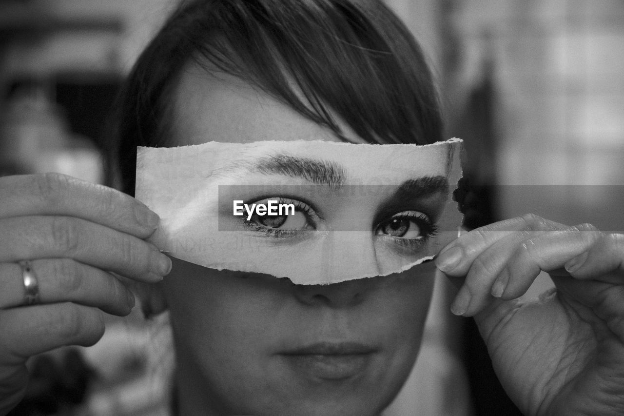 Close-up of woman holding torn paper eyes over face