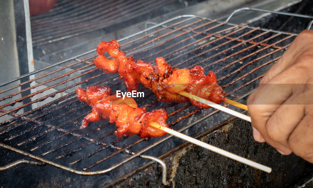 Cropped hand of man preparing meat on barbecue grill