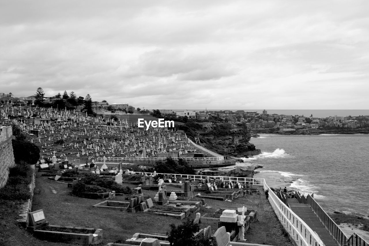 Cemetery by sea against cloudy sky