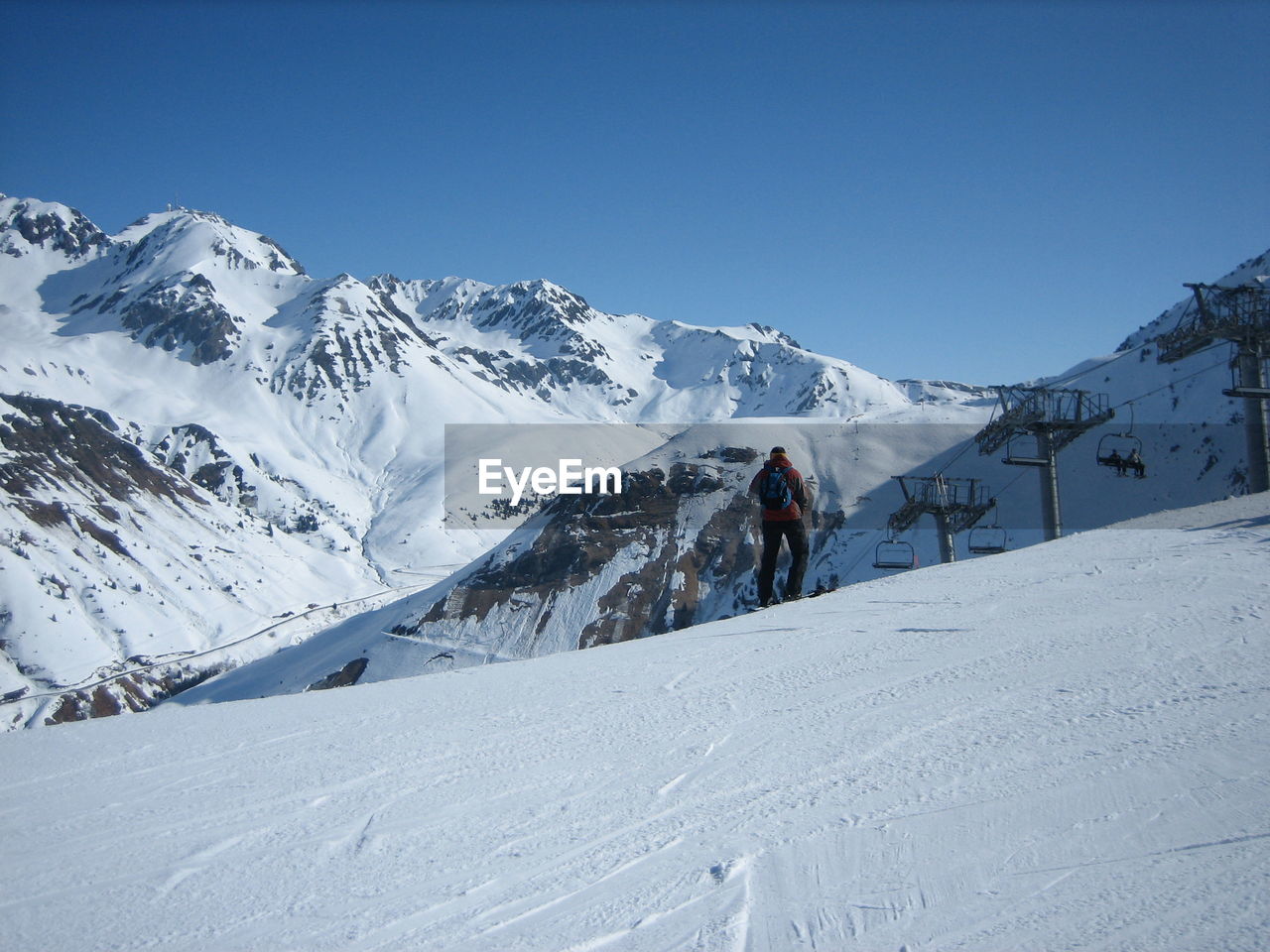 Rear view of snowboarder on snowcapped mountain against clear sky