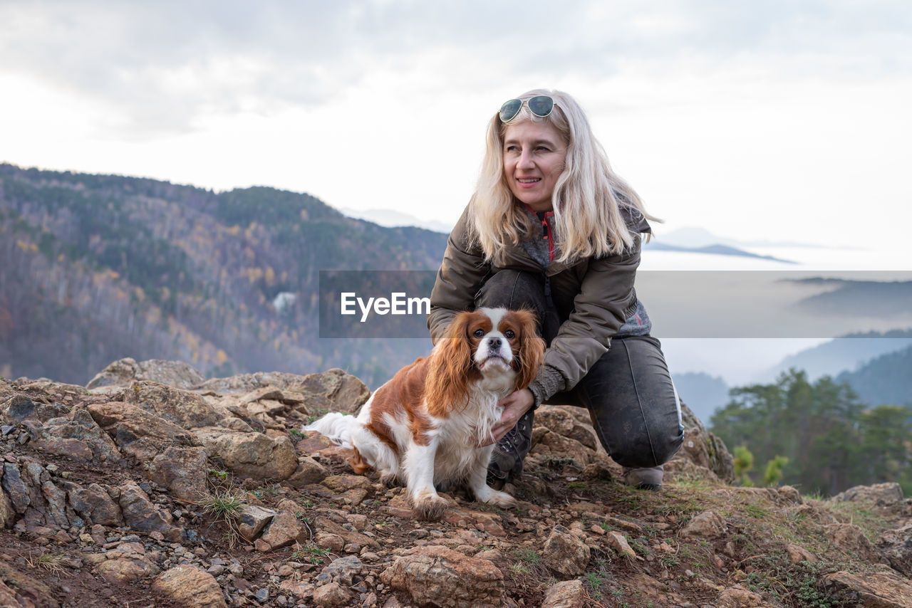 Blond woman and her cavalier king charles spaniel on a mountain top on a hazy day