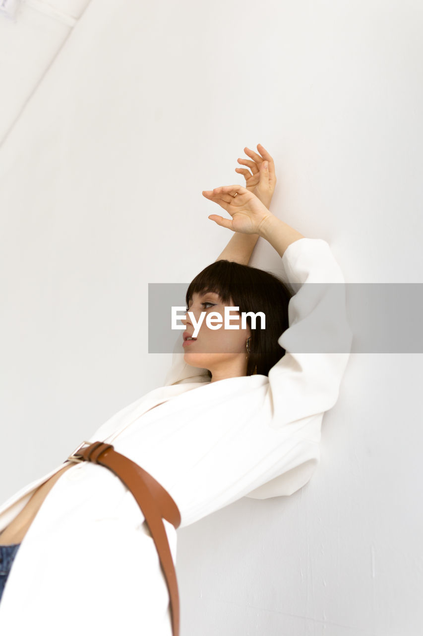 PORTRAIT OF A YOUNG WOMAN LOOKING DOWN AGAINST WHITE WALL