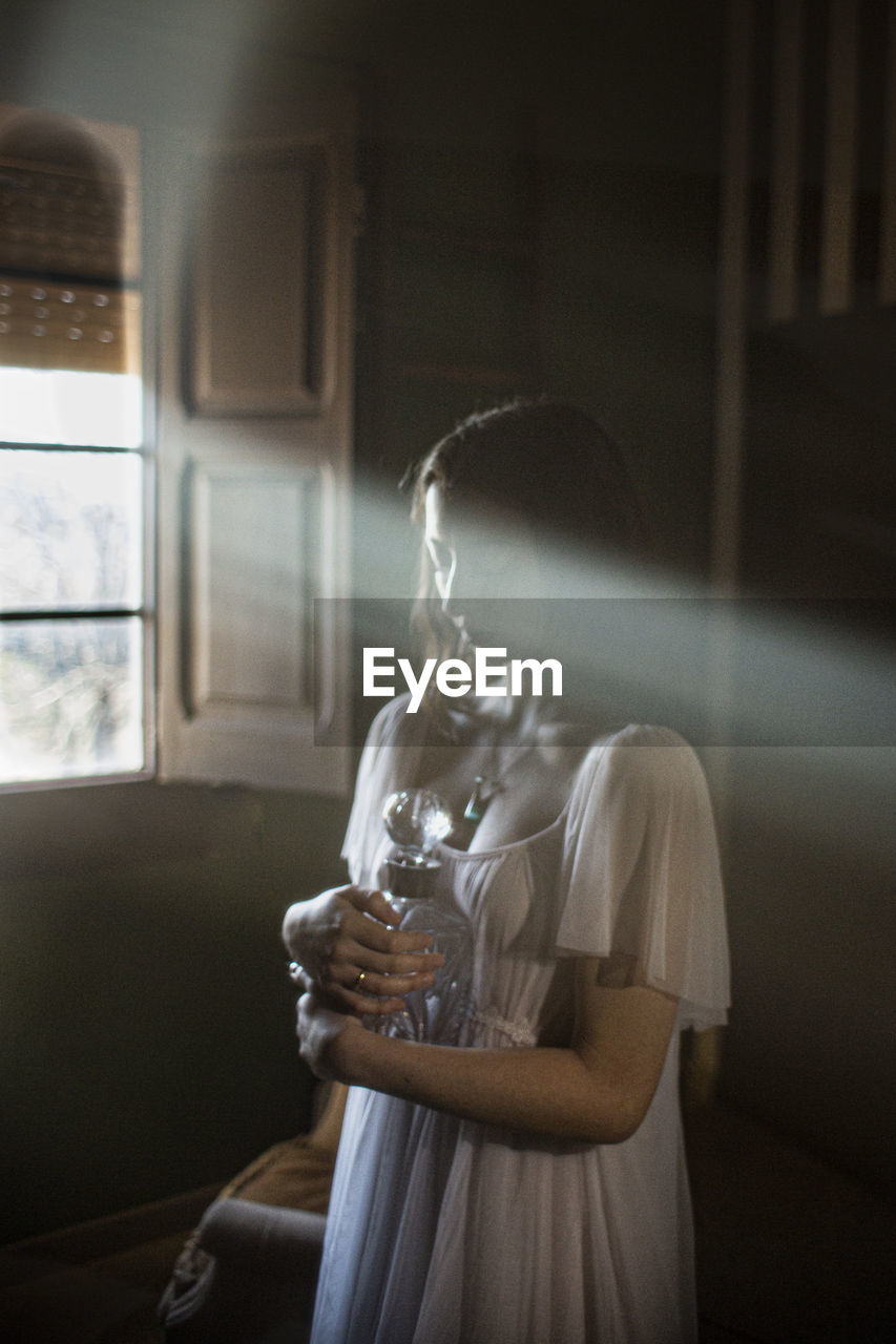 Young woman holding glass jar standing at home