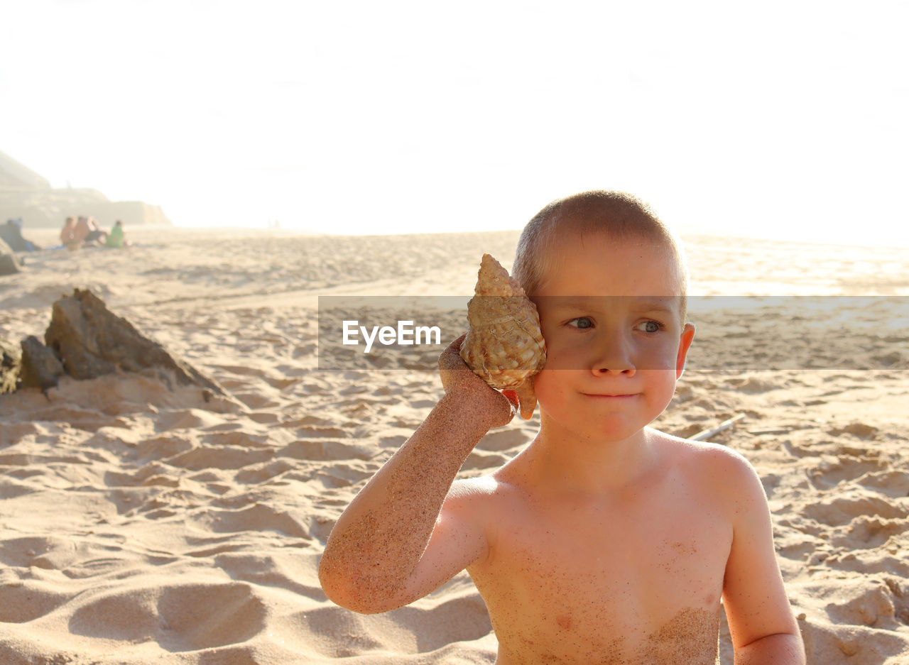 Pensive boy on the beach with a sea shell in his hand. a six-year-old boy purses his lips  