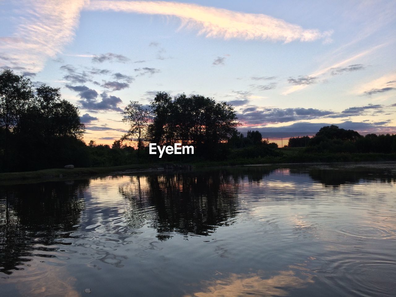 REFLECTION OF SILHOUETTE TREES IN LAKE AGAINST SKY