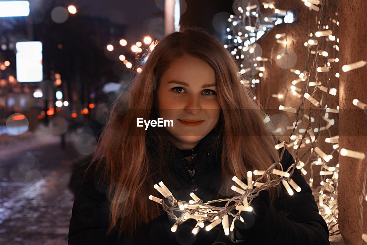 Portrait of beautiful woman standing by illuminated lights