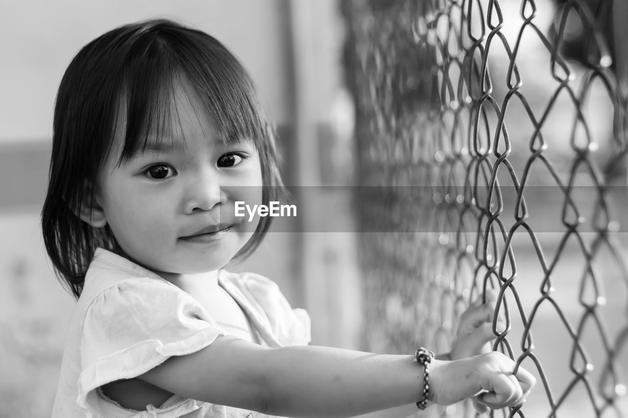 Portrait of baby girl standing by chainlink fence