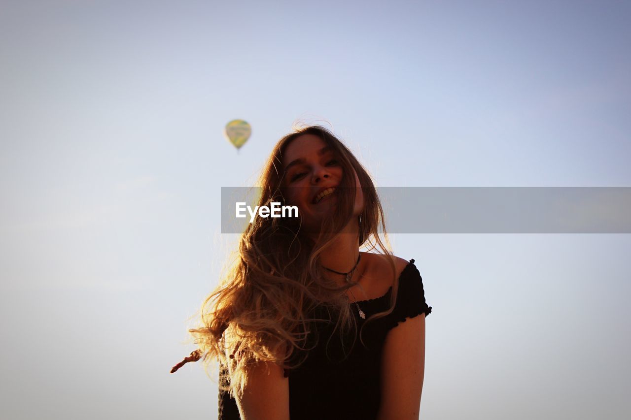 Low angle view of smiling young woman against hot air balloon