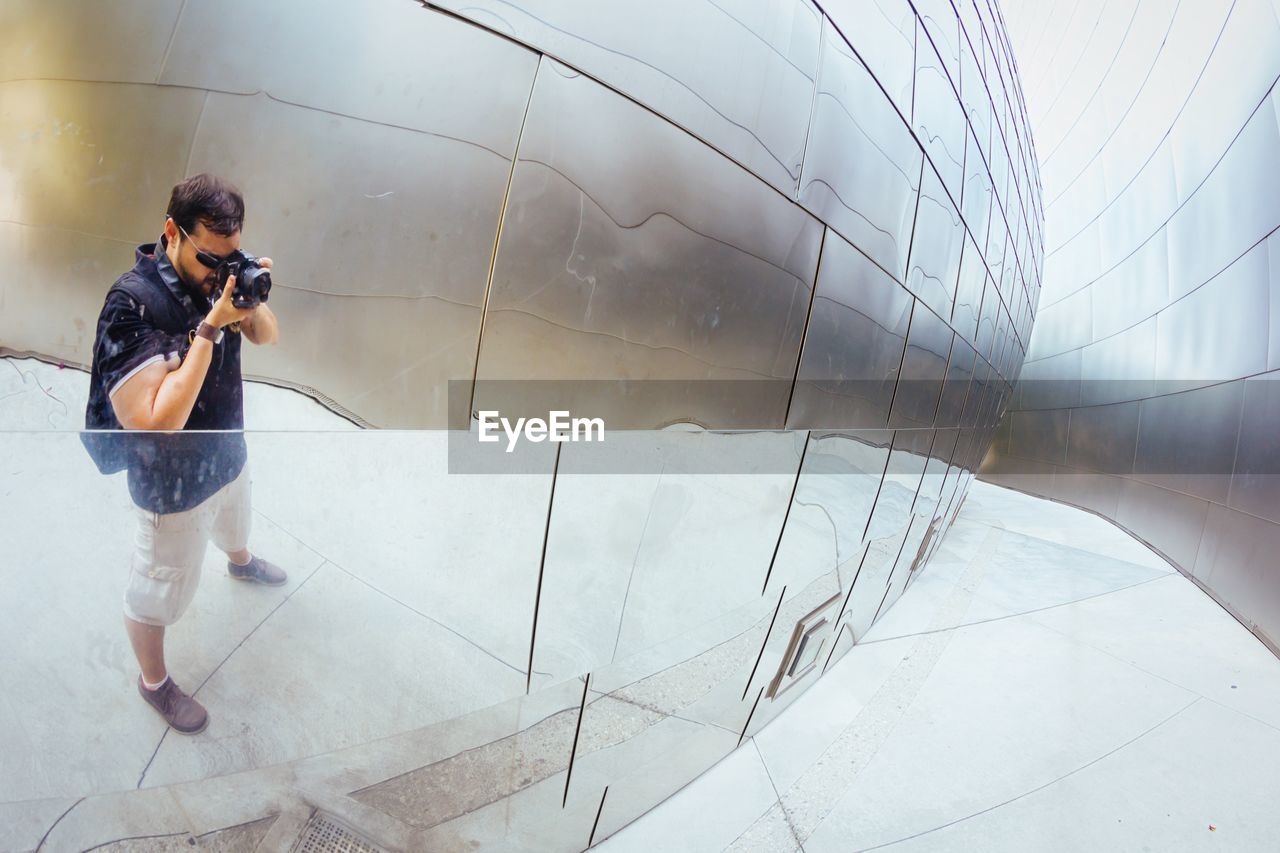 Man photographing through camera reflecting on glass wall