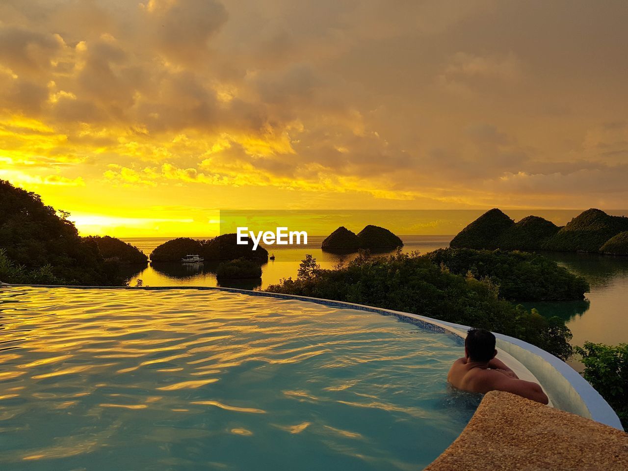 Man swimming in infinity pool by sea against sky during sunset