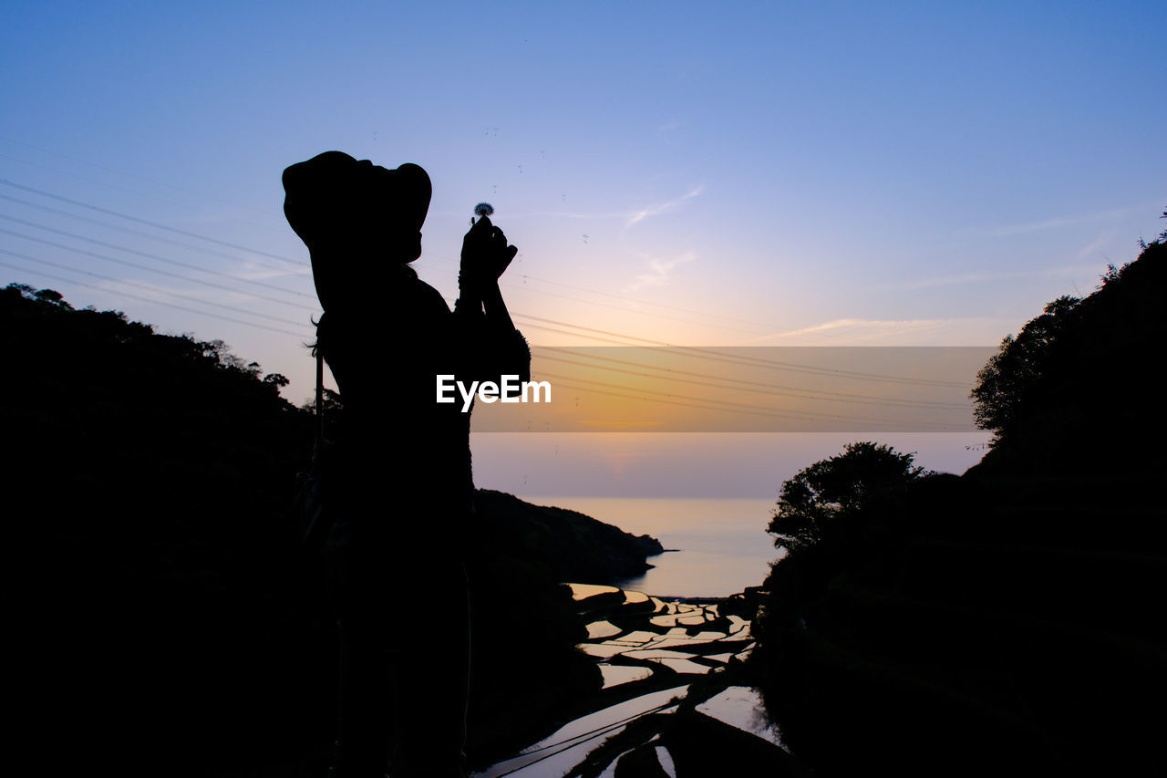 low angle view of silhouette woman standing on mountain against sky during sunset