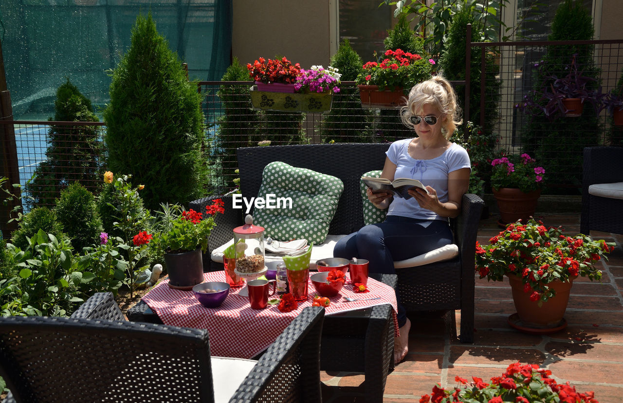 Woman reading a book by a set table in a lush garden