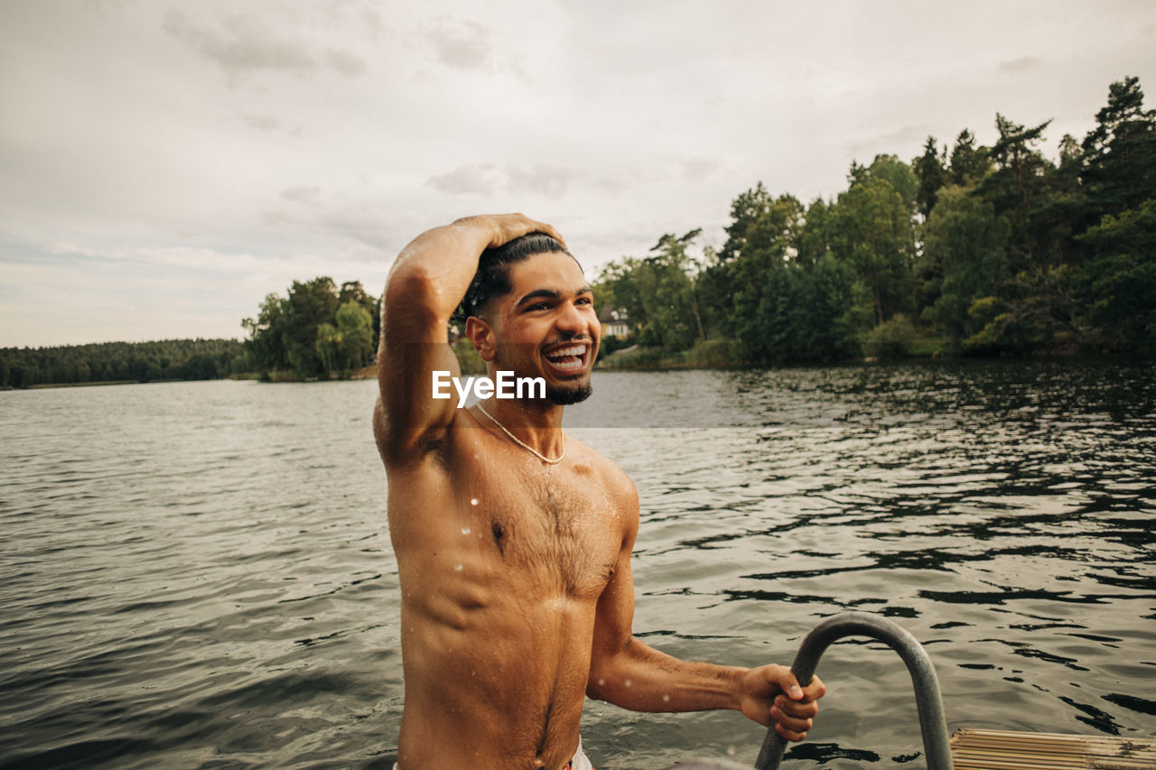 Happy shirtless man with head in hand enjoying swimming at lake during vacation
