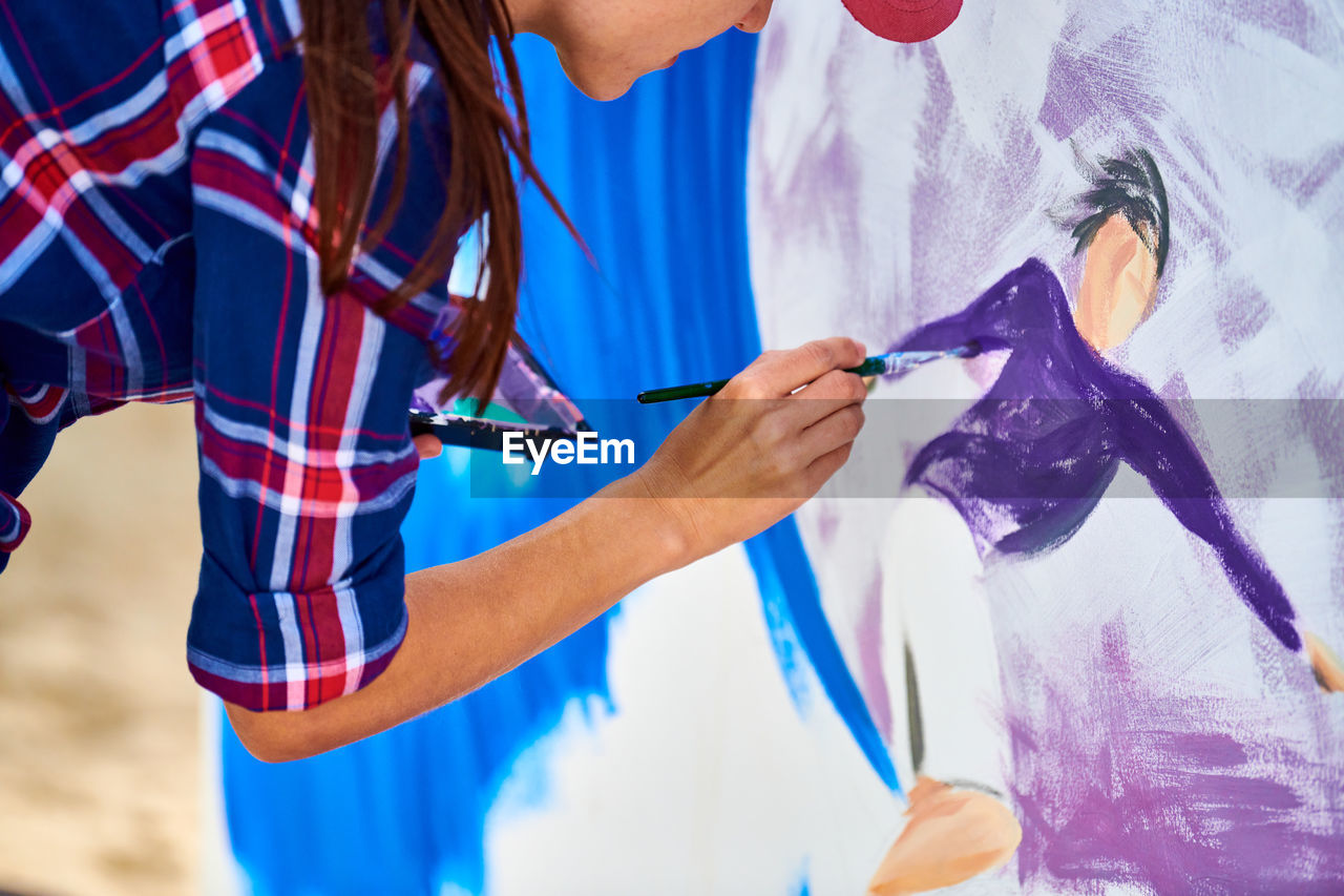 Female artist painting on wooden canvas board at outdoor festival, young adult painting picture