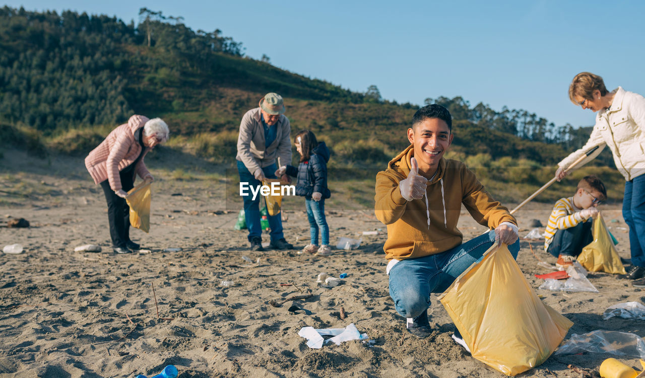 Portrait of man with family cleaning beach against mountain