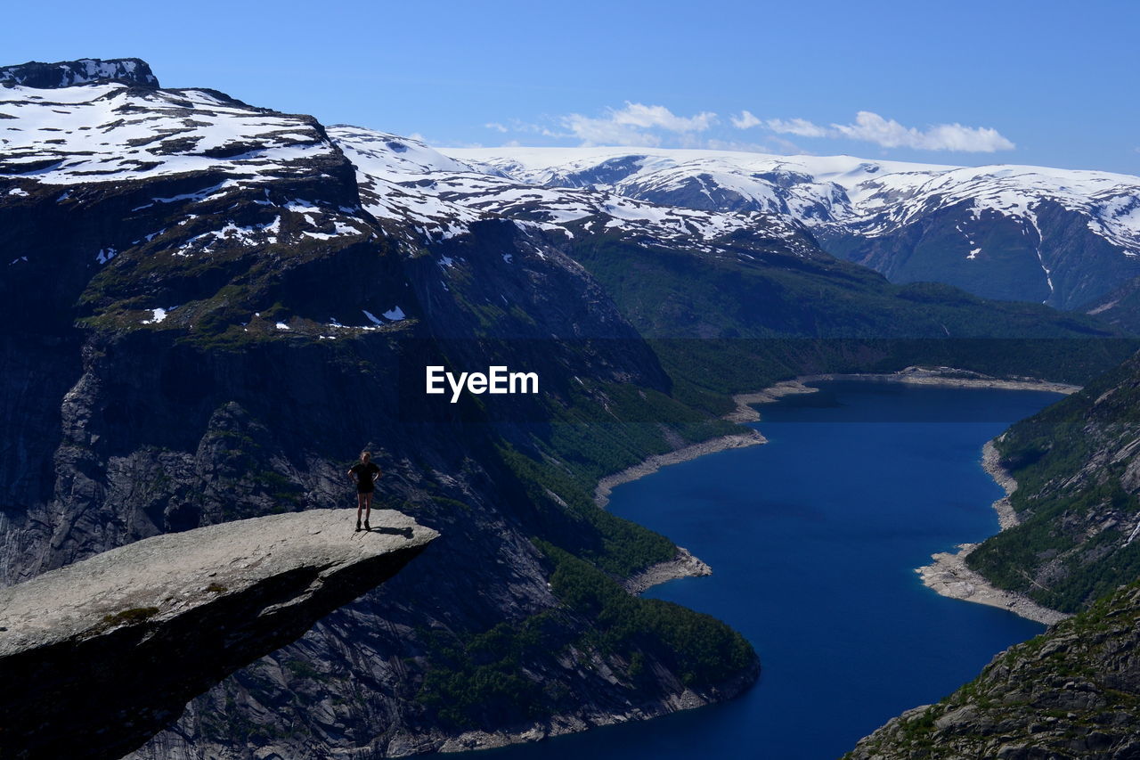 High angle view of person standing at trolltunga against snowcapped mountains