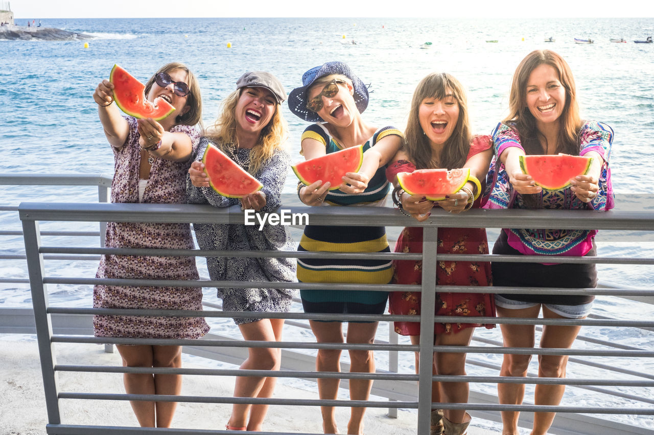 Group of female friends holding watermelon while standing on bridge