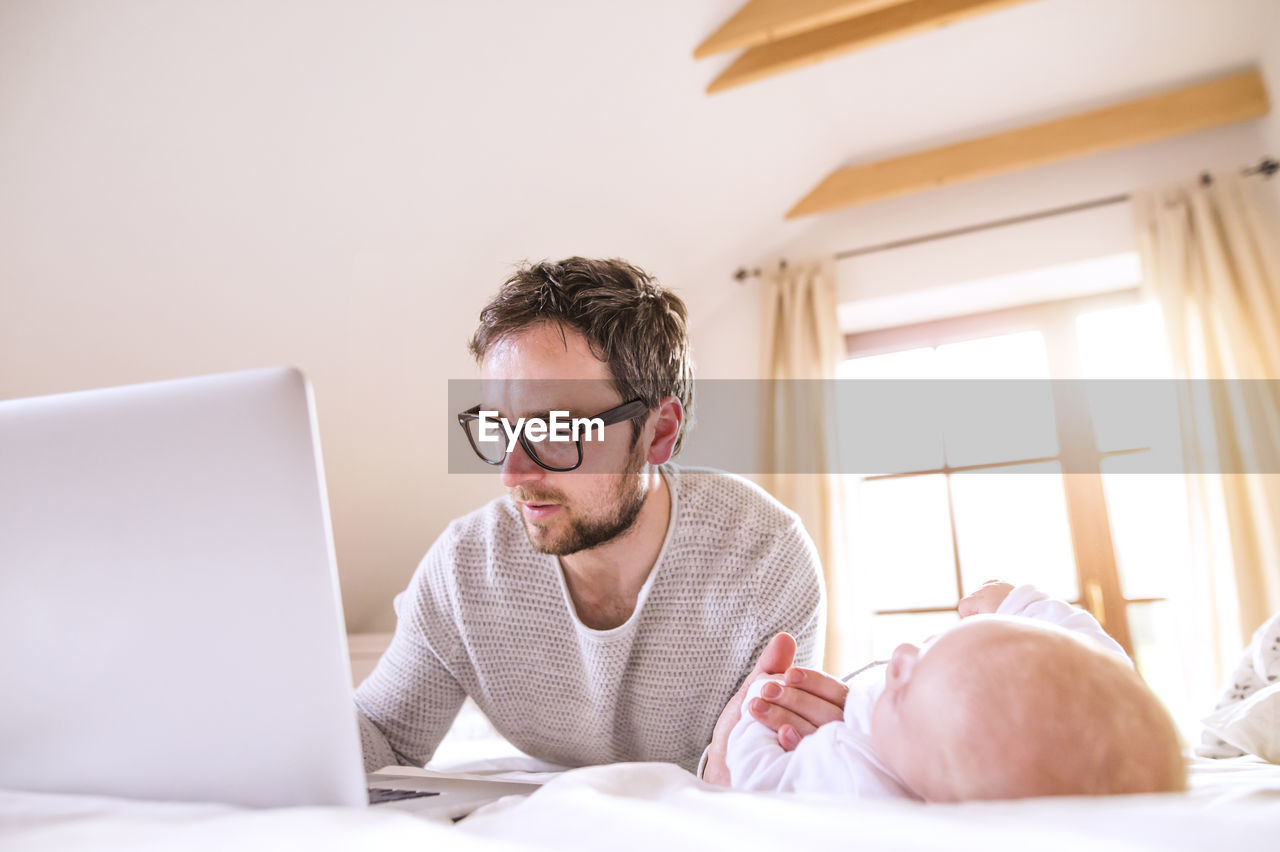 Father with baby lying on bed using laptop