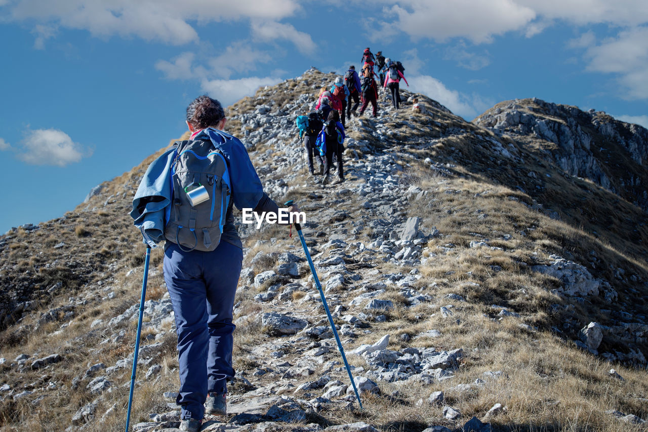 Group of hikers walk on the mountain path, helping themselves up the climb with trekking poles.