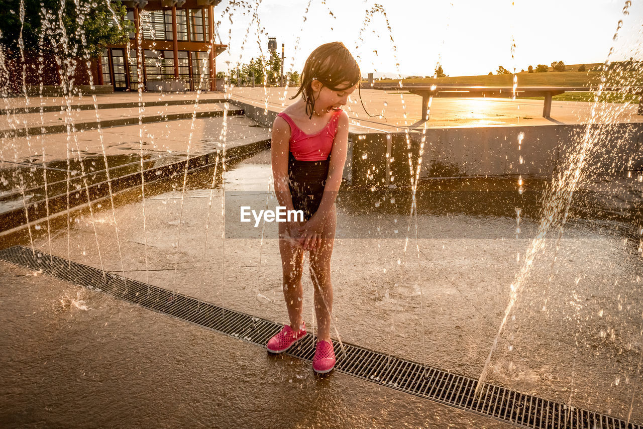 Joyful young girl in bathing suit plays at a splash pad at sunset