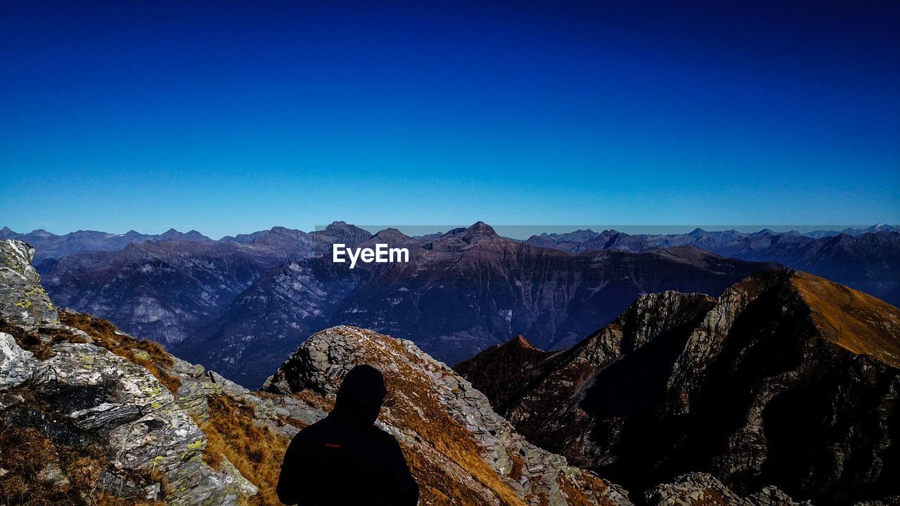 REAR VIEW OF PERSON ON ROCK AGAINST SKY