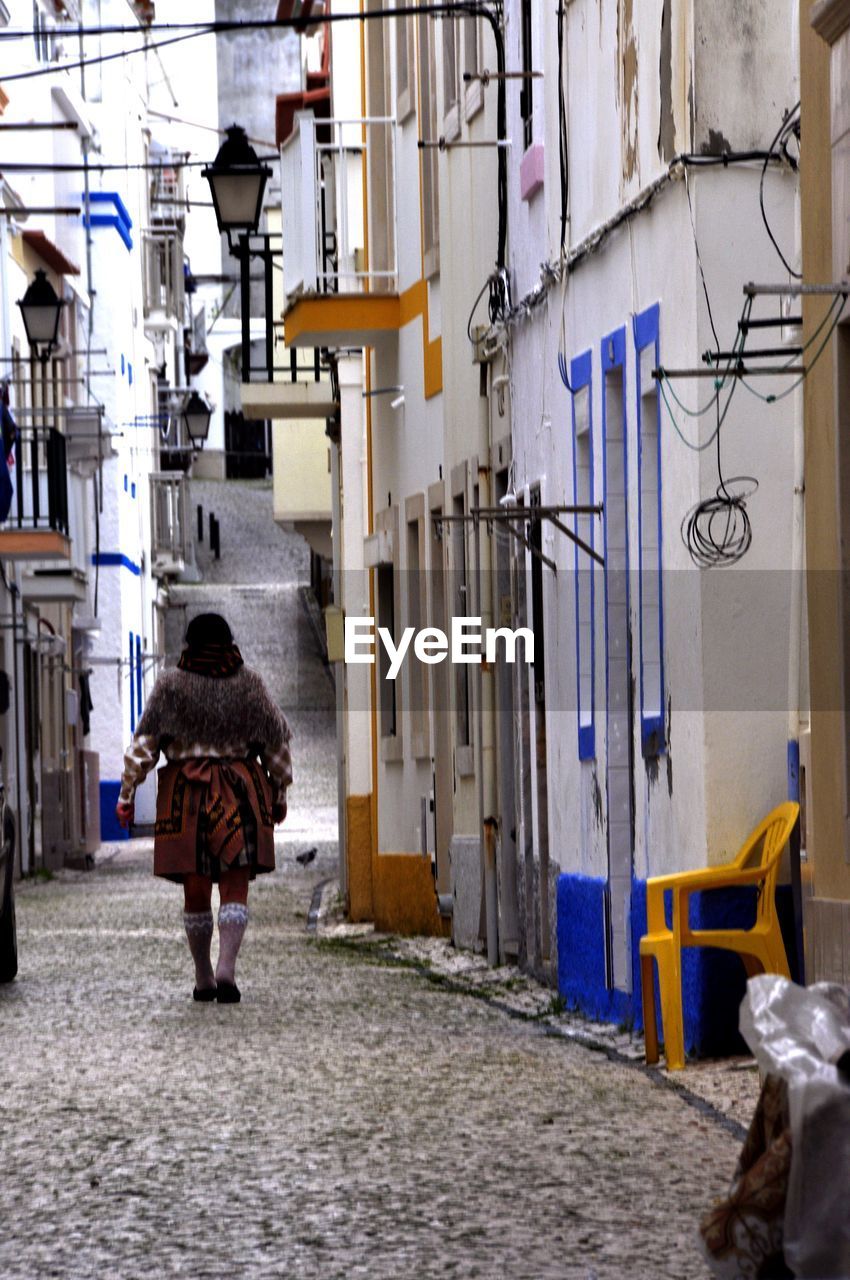 Rear view of woman walking on footpath amidst buildings