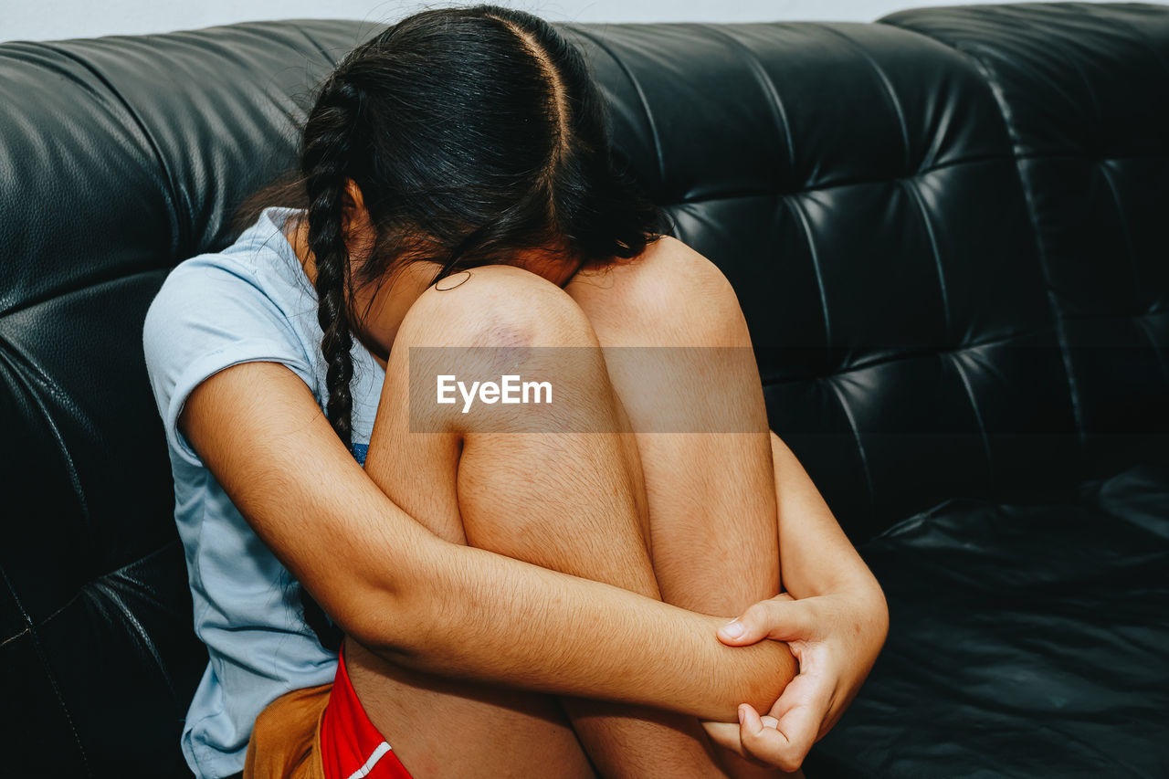 Girl hugging knees sitting on sofa at home