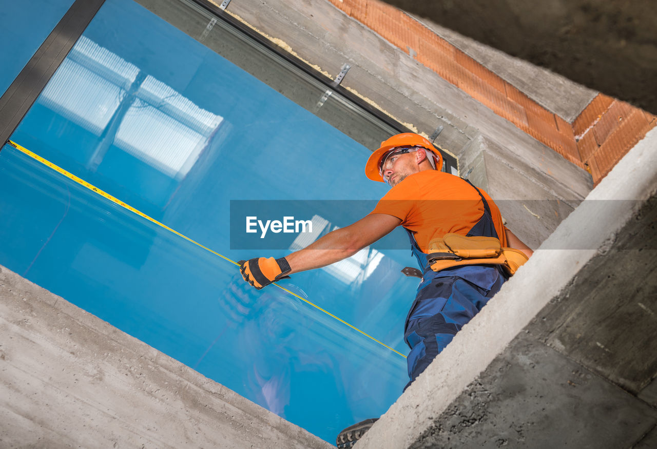HIGH ANGLE VIEW OF MAN WORKING AT ORANGE CONSTRUCTION SITE