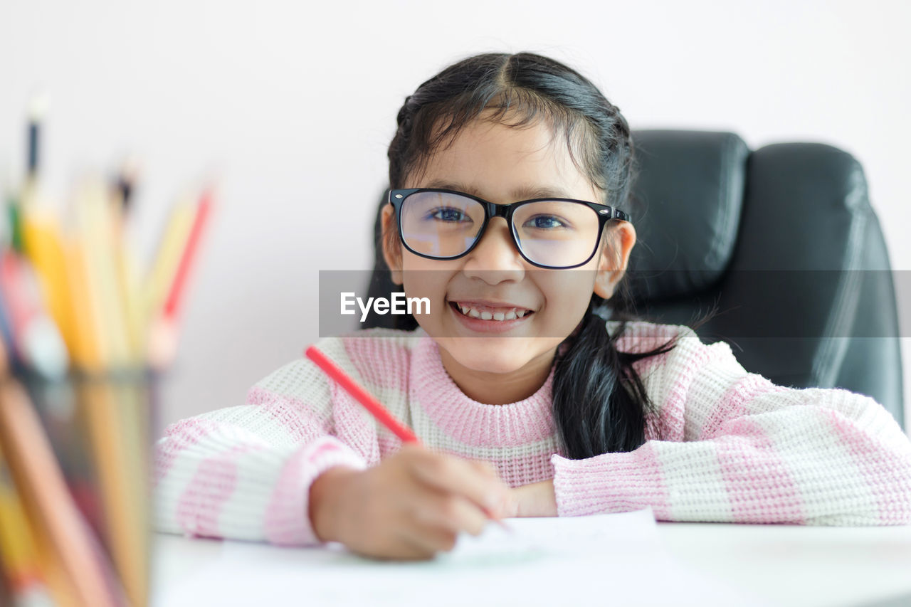 Portrait of smiling girl writing in paper against white background