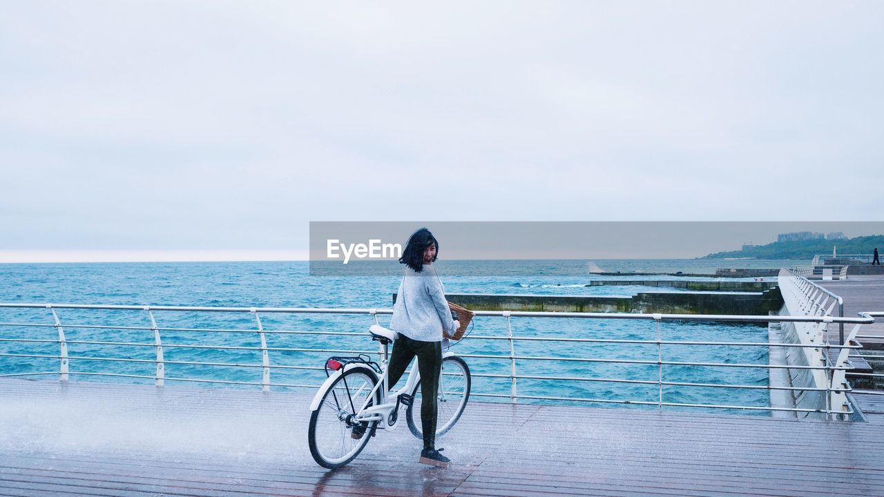 Woman with bicycle standing on promenade against sky