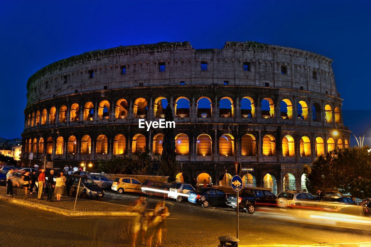 Blurred motion of tourists on street against coliseum during night