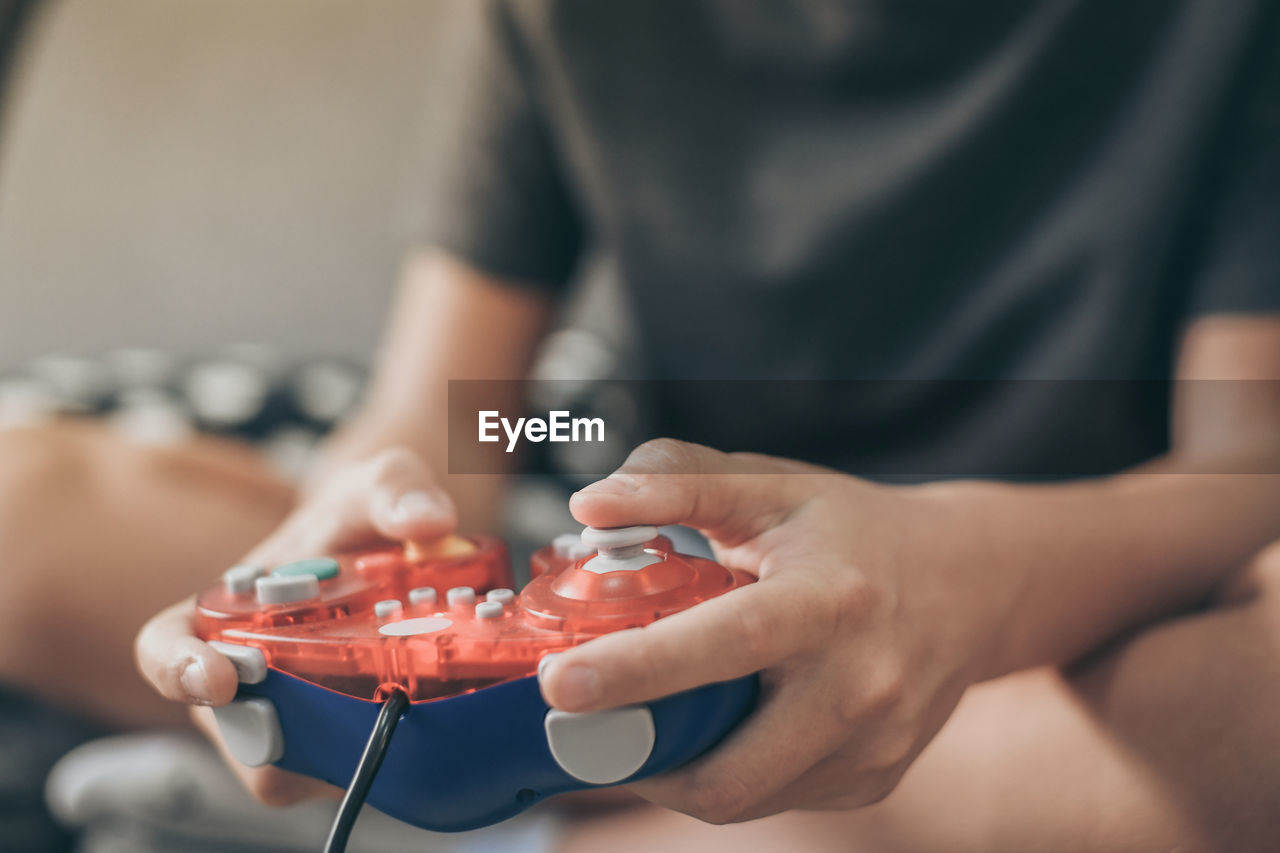 Midsection of boy holding game controller at home