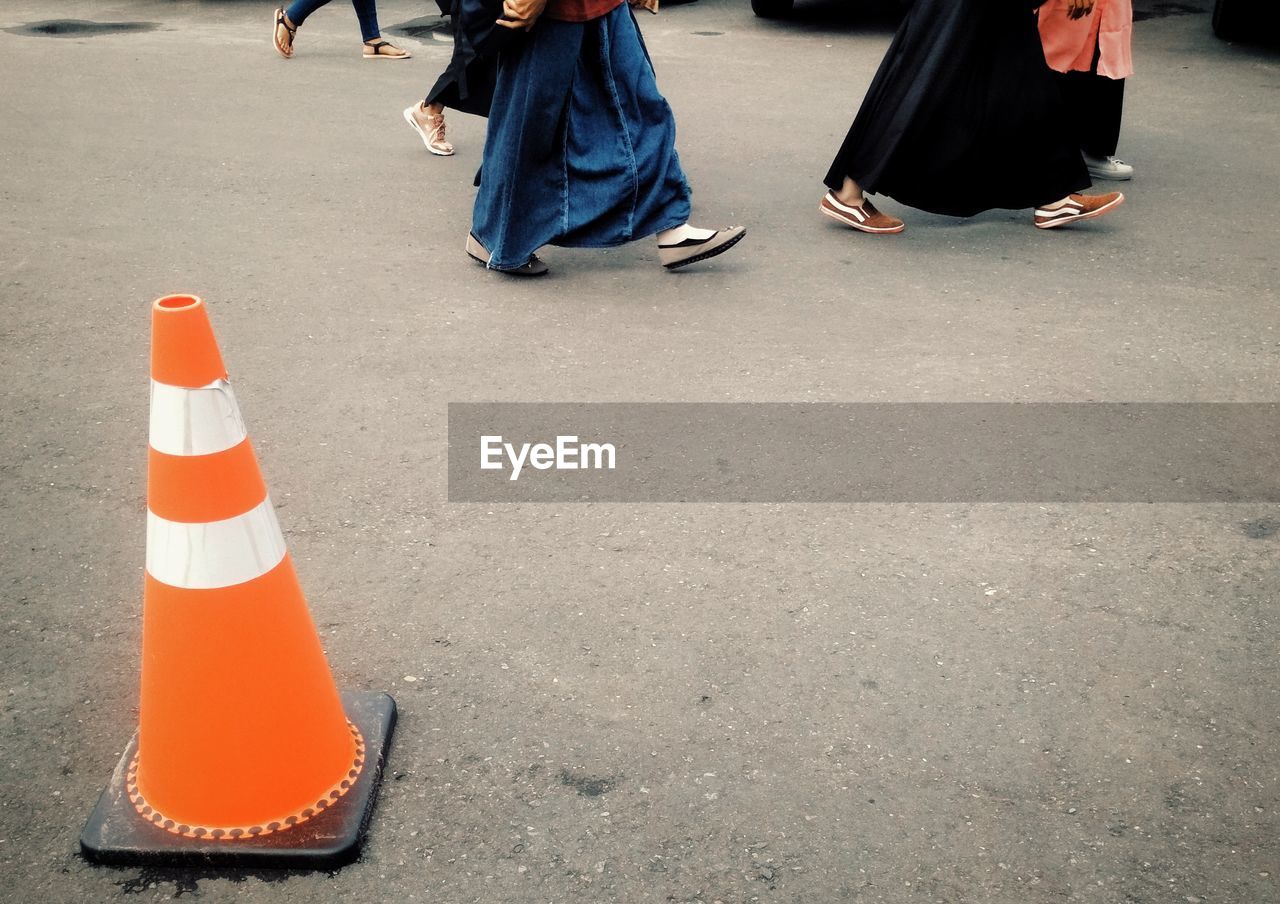 Low section of people walking by traffic cone on road