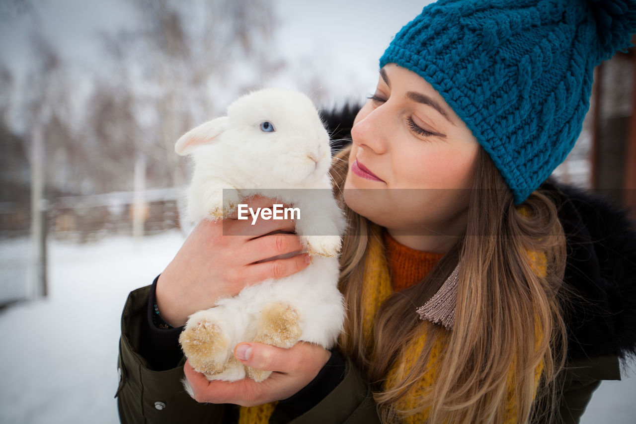 Close-up of woman holding rabbit while standing on field during winter