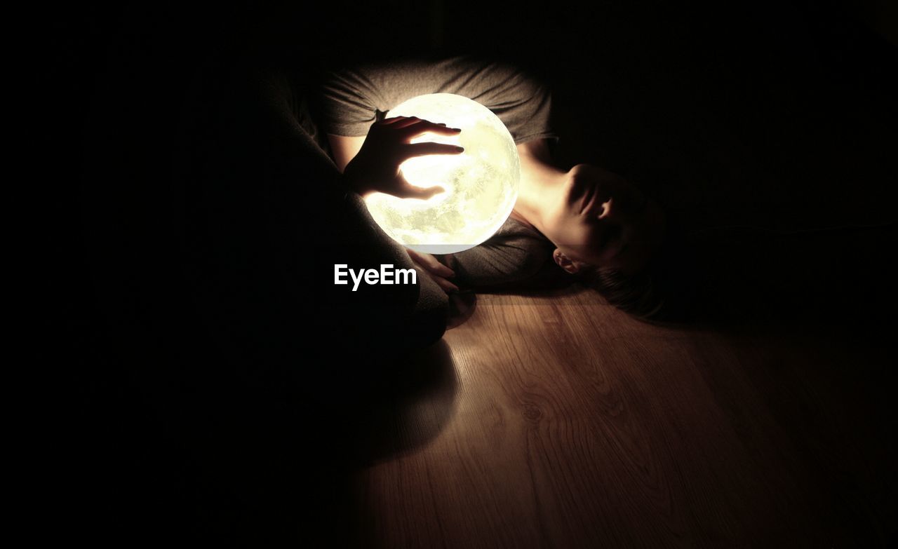 Woman holding illuminated ball and lying down on floor