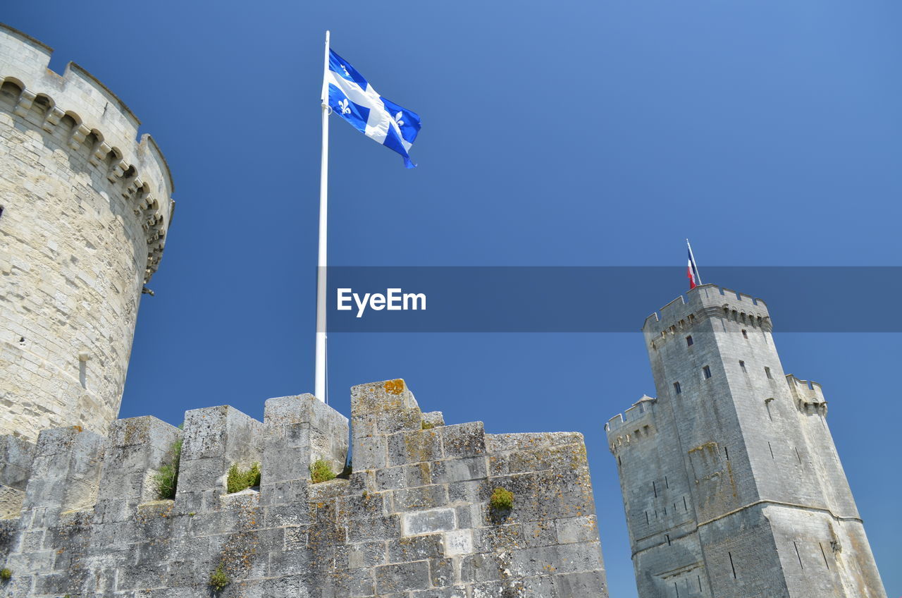 Low angle view of flags against blue sky on tower of la rochelle, france.