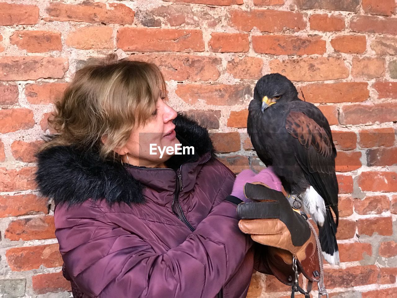 Woman holding bird against brick wall