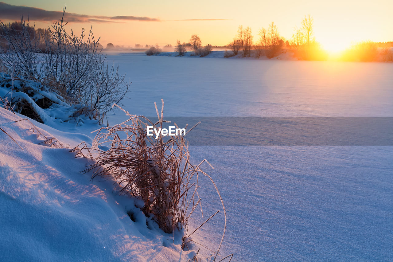 The sun rises over the icy river at the rural finland. the sunlight colors the frosty scenery amber.