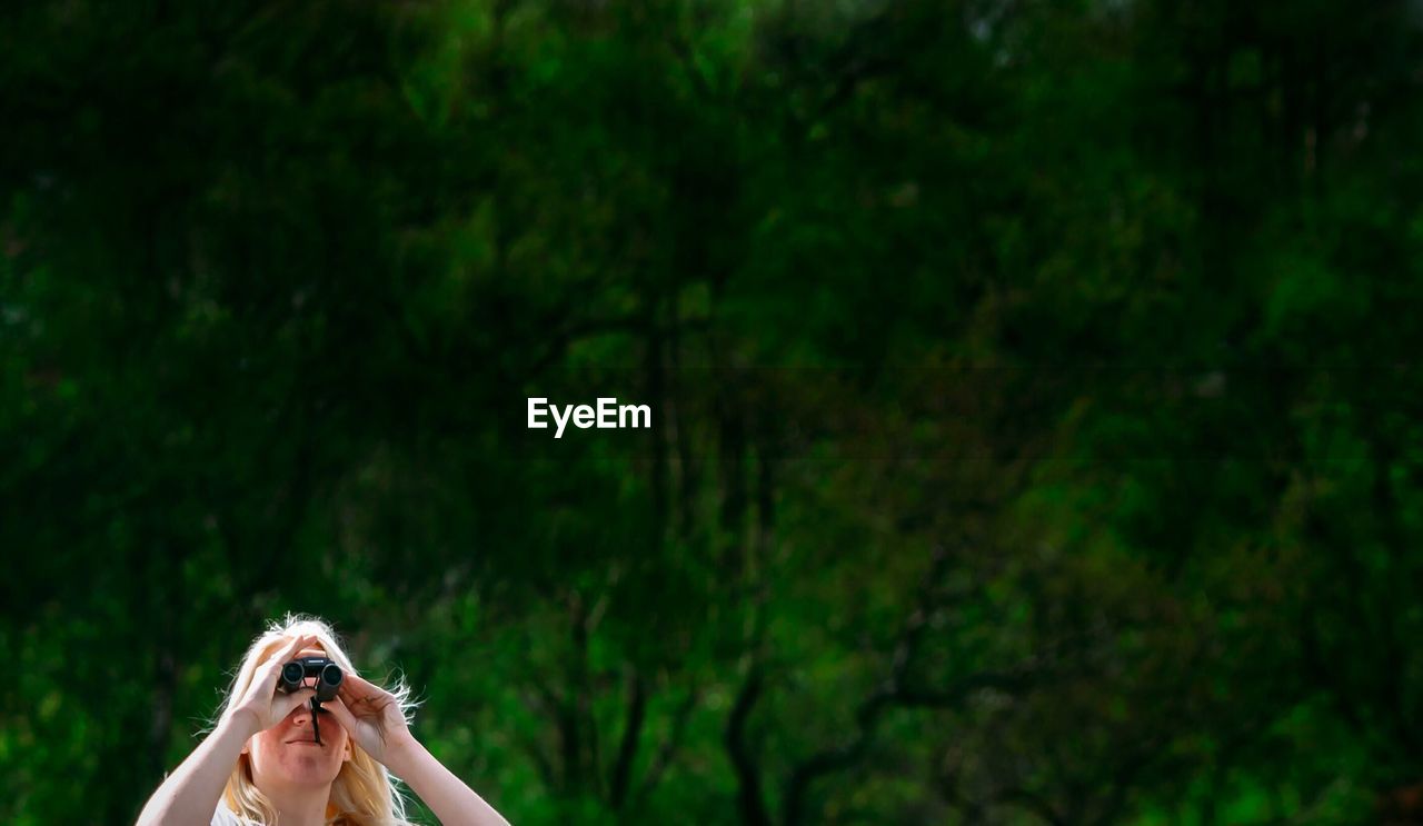 Woman looking through binoculars against trees