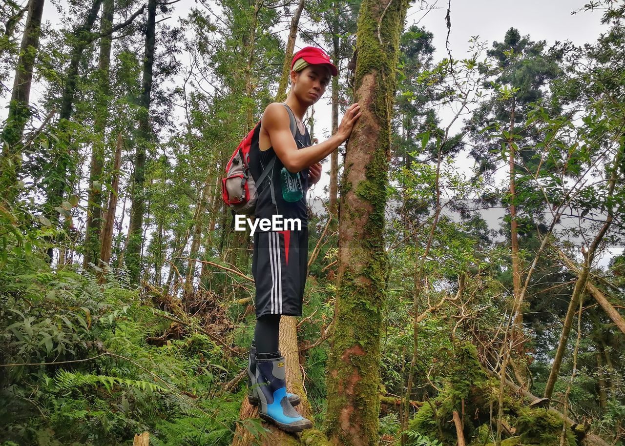 YOUNG MAN STANDING BY TREE IN FOREST