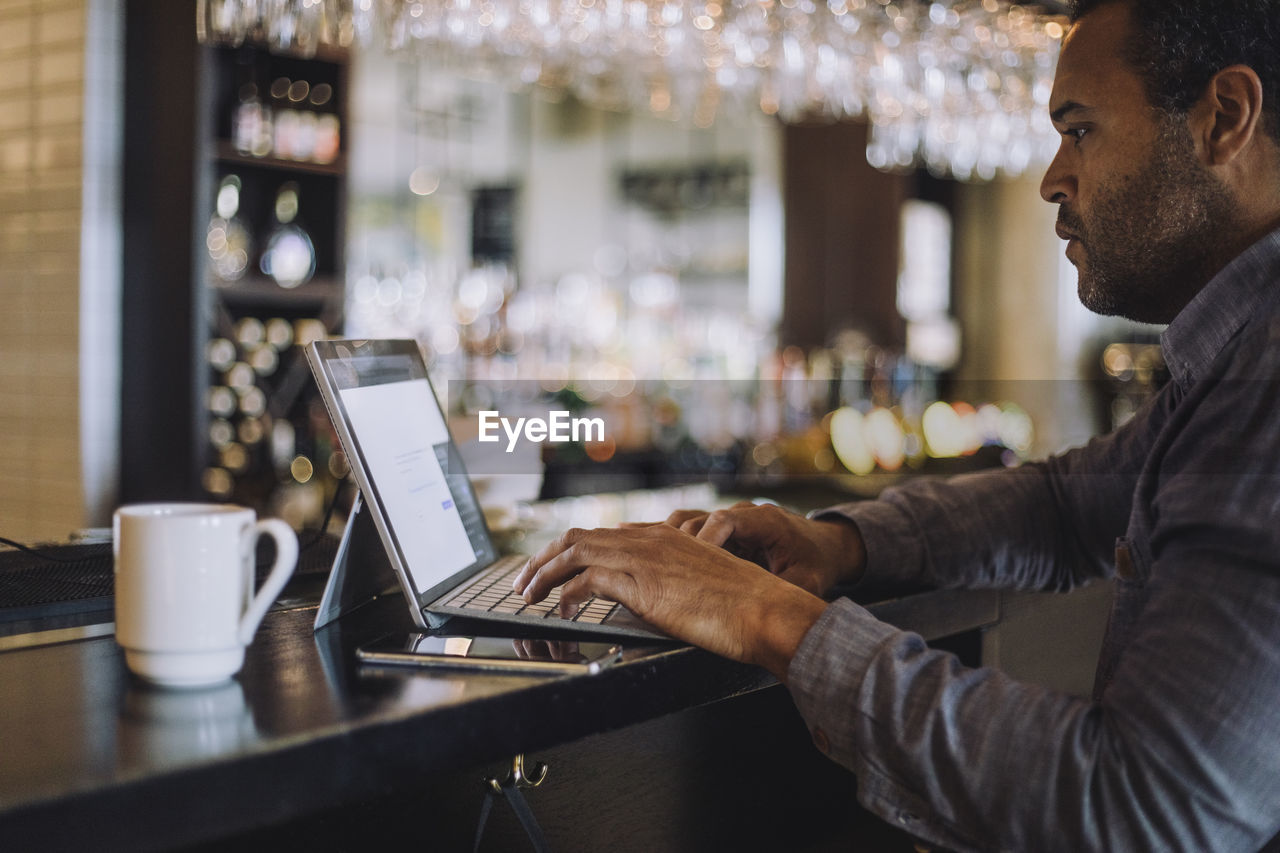 Side view of male entrepreneur using laptop at bar counter in restaurant