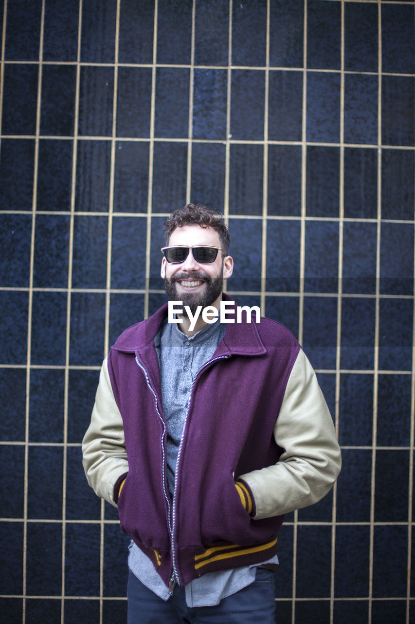 Portrait of smiling man with hands in pocket standing against pattern wall