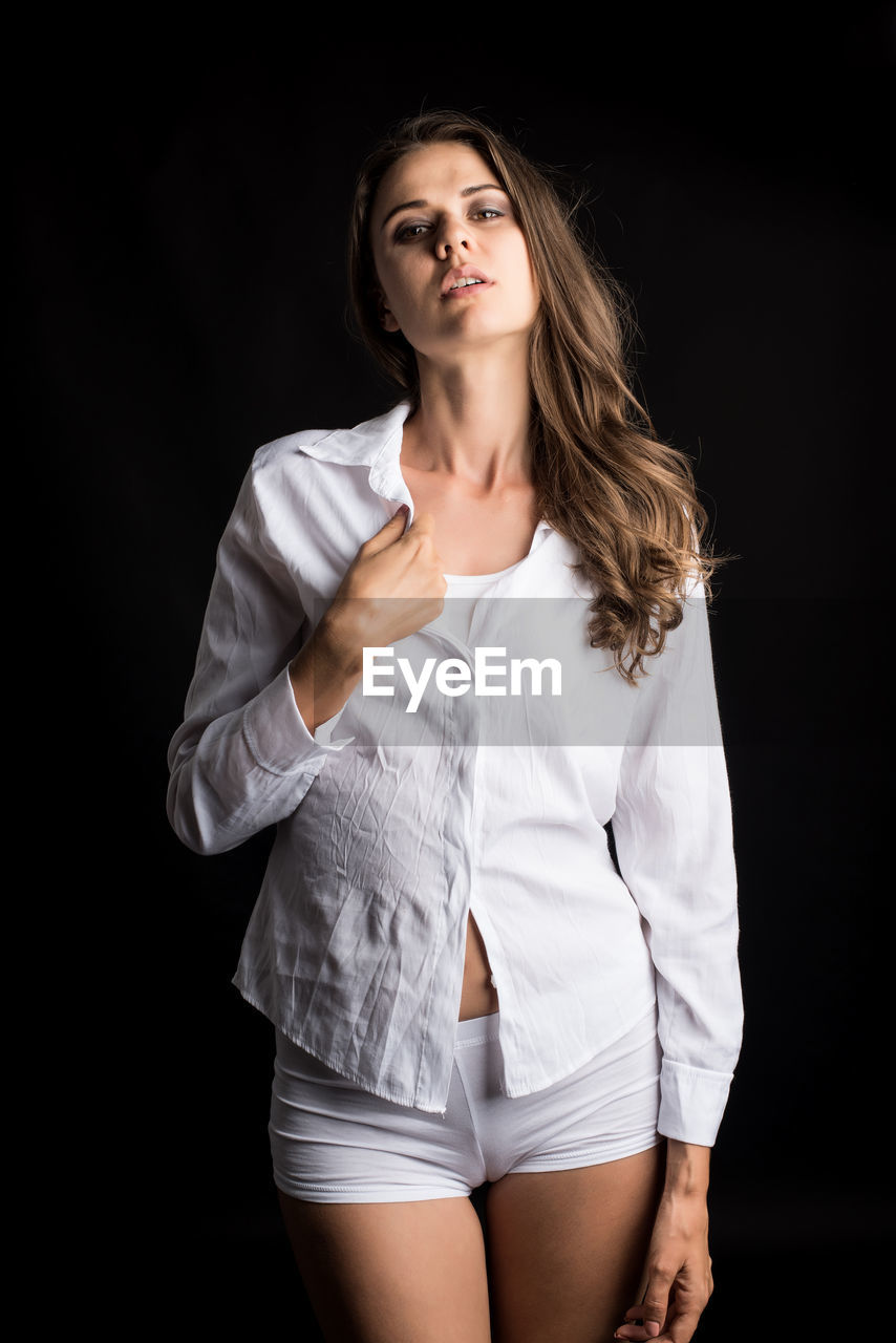 PORTRAIT OF BEAUTIFUL WOMAN STANDING AGAINST BLACK BACKGROUND