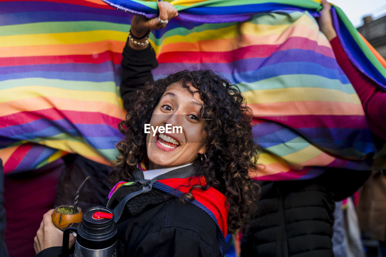 Woman looking at camera while holding a rainbow flag in an lgbtq pride march.