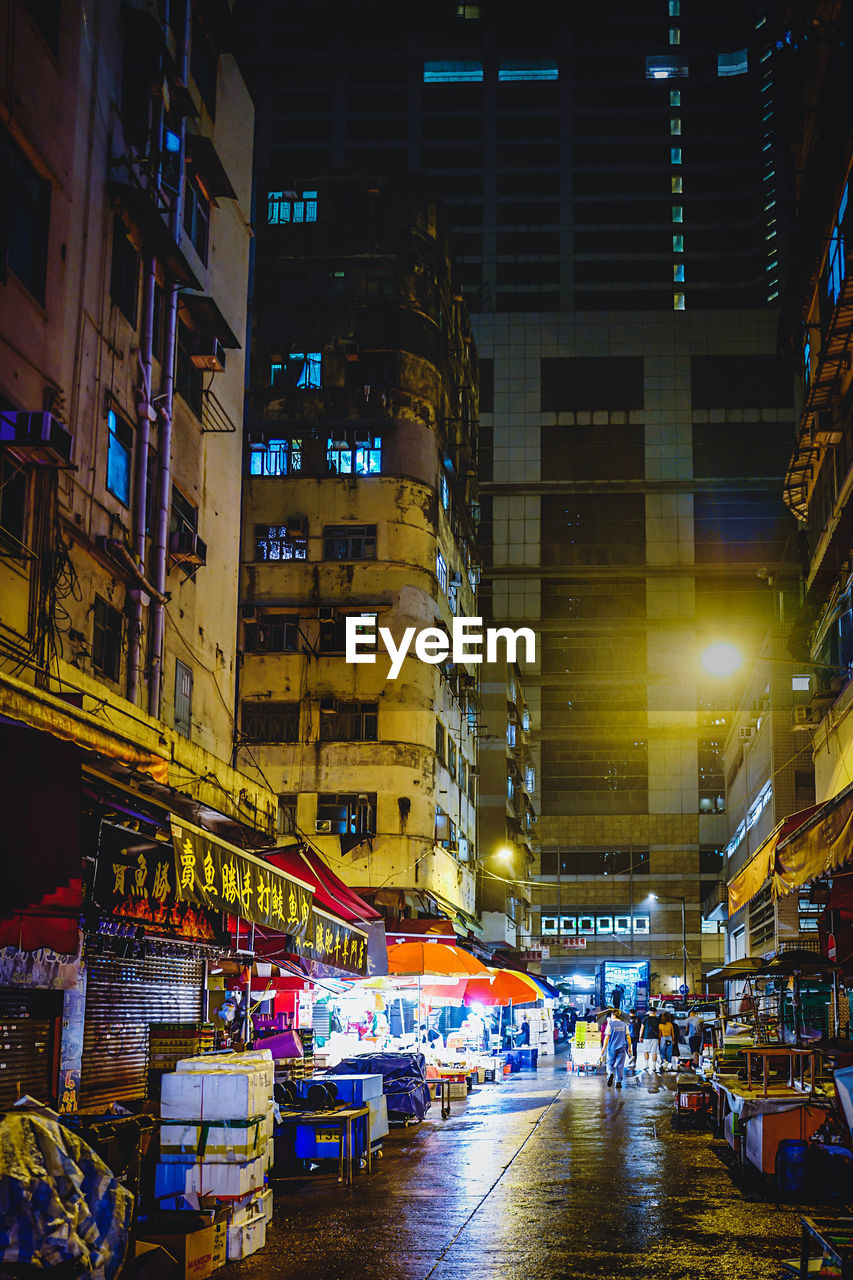 ILLUMINATED STREET MARKET AMIDST BUILDINGS AT NIGHT