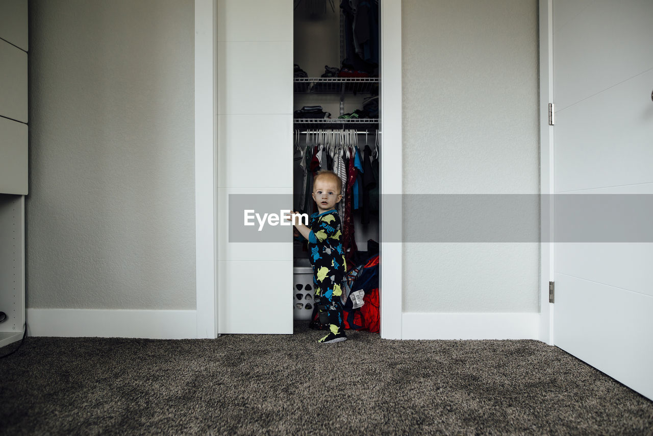 Portrait of baby boy standing at closet